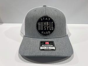 Stay Humble Hustle Hard Hat Leatherette patch hat is a Richardson 112 Trucker Hat with adjustable snapback.